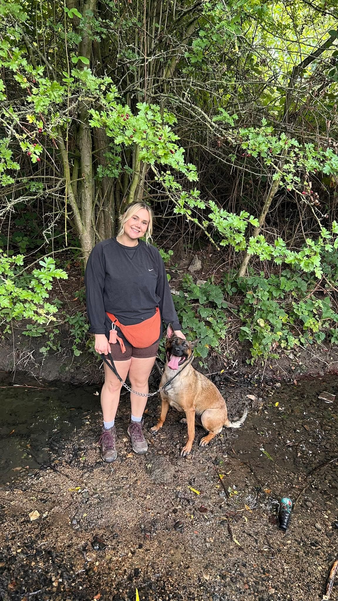 Amelia standing outdoors by trees with Maple the dog sitting beside her on a lead.