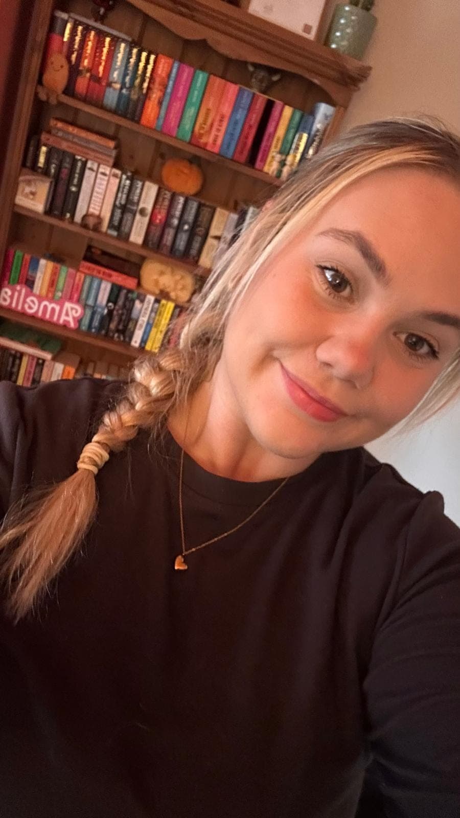 Amelia smiling at the camera in front of a bookcase, her hair in a plait.