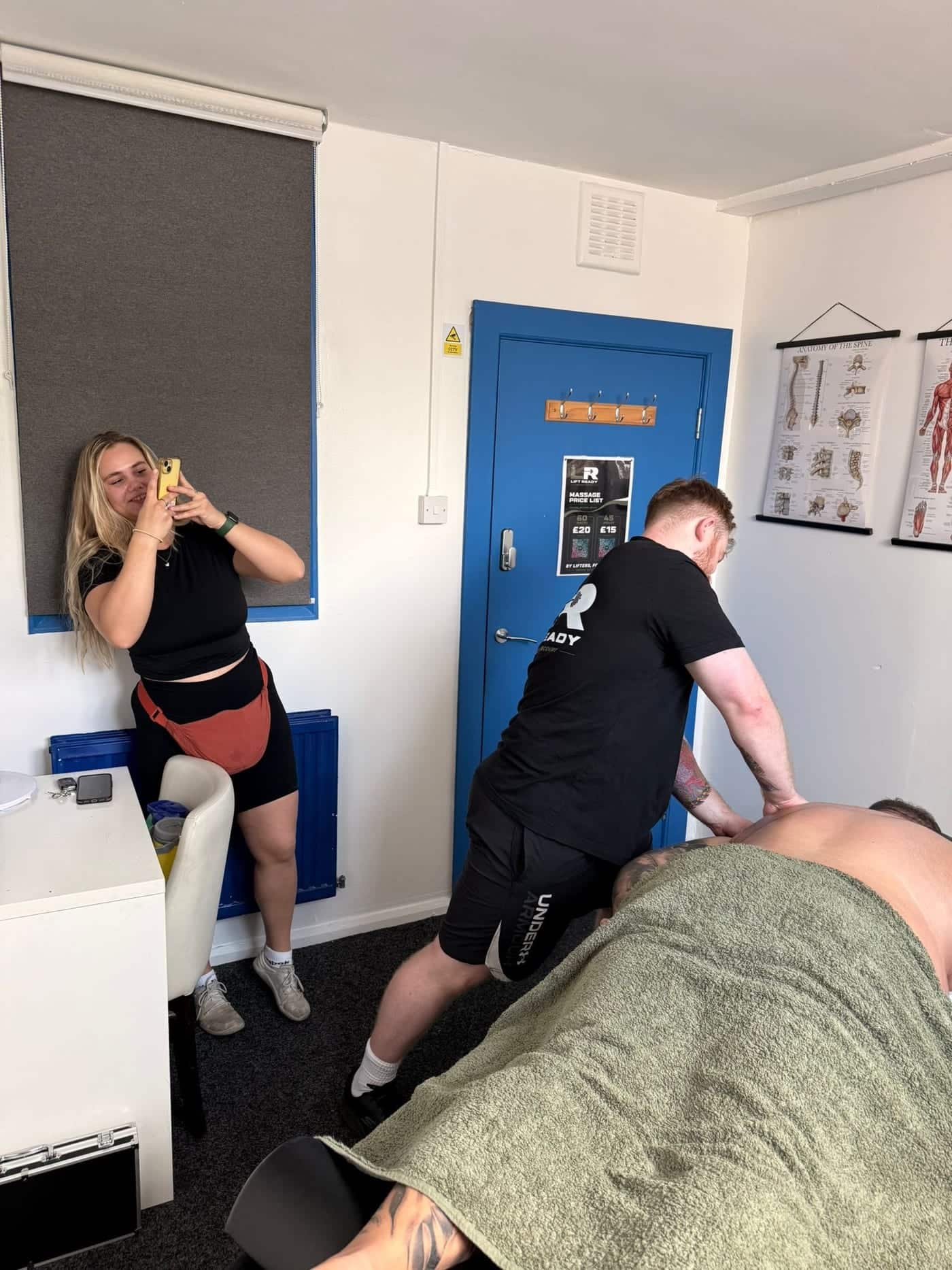 Amelia smiling as she films on her phone while a Lift Ready therapist works on a client's back.