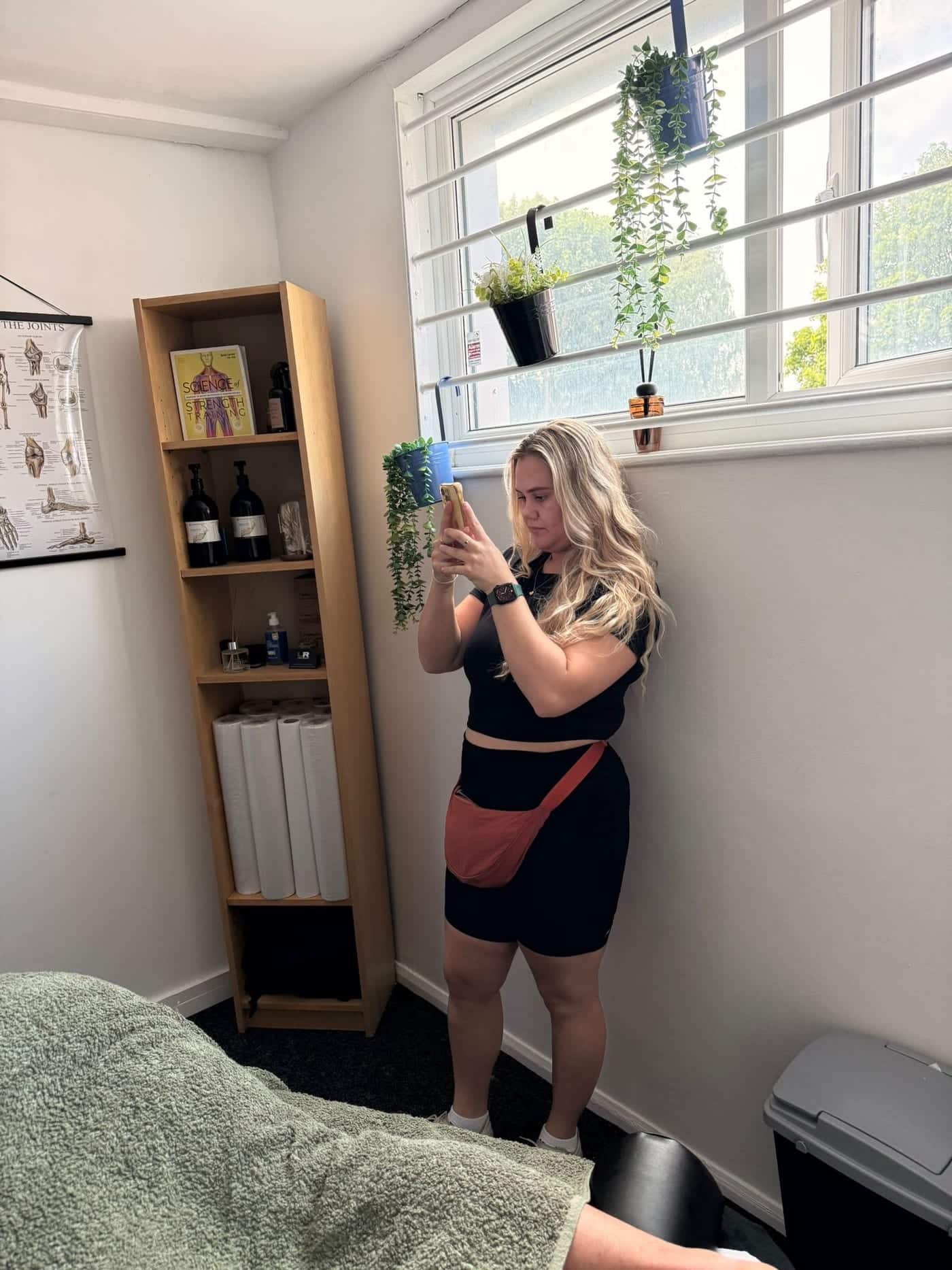 Amelia by a window in a treatment room, filming on her phone.