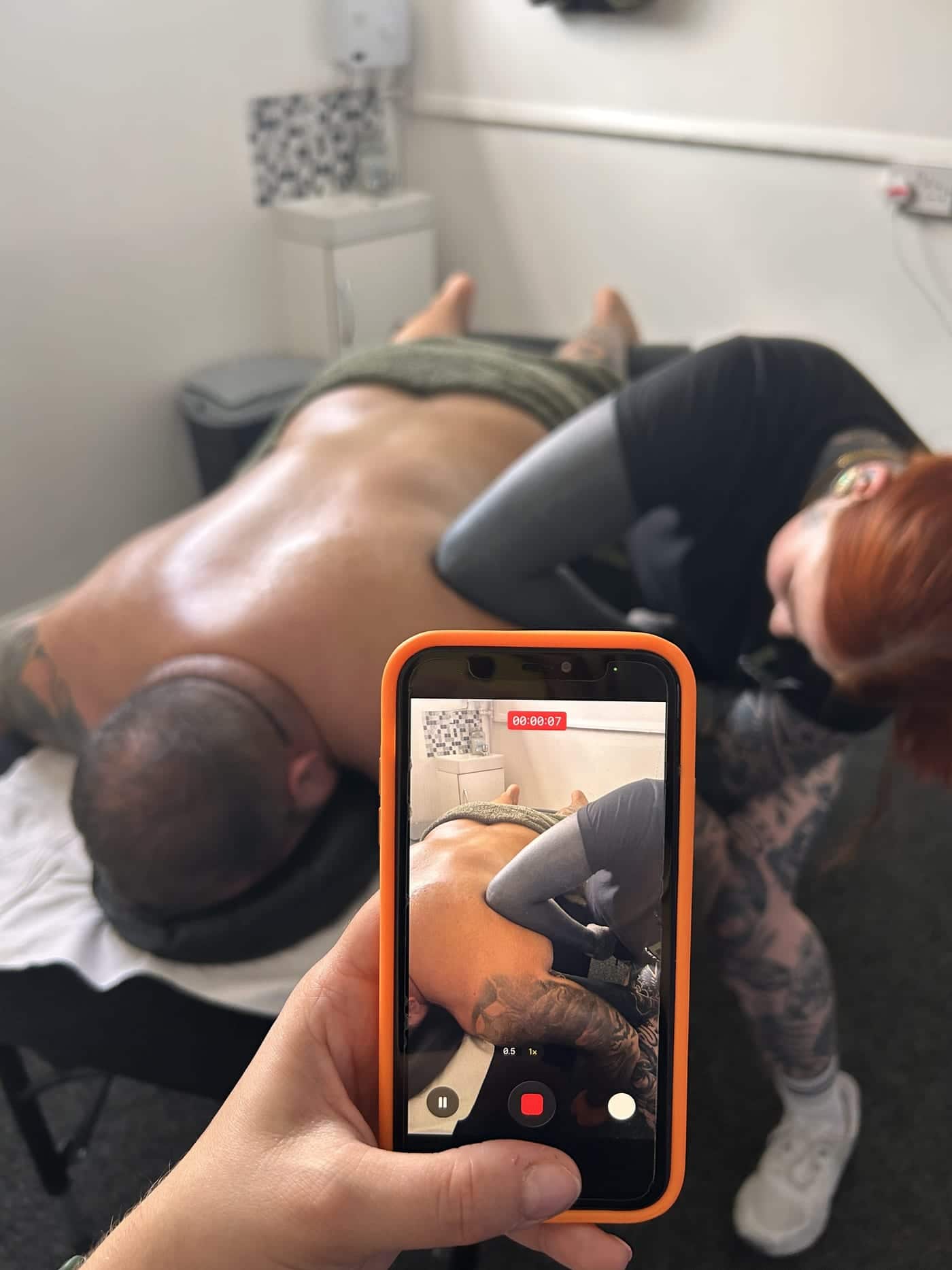 Amelia's hand holding an orange phone that is recording a therapist at work.